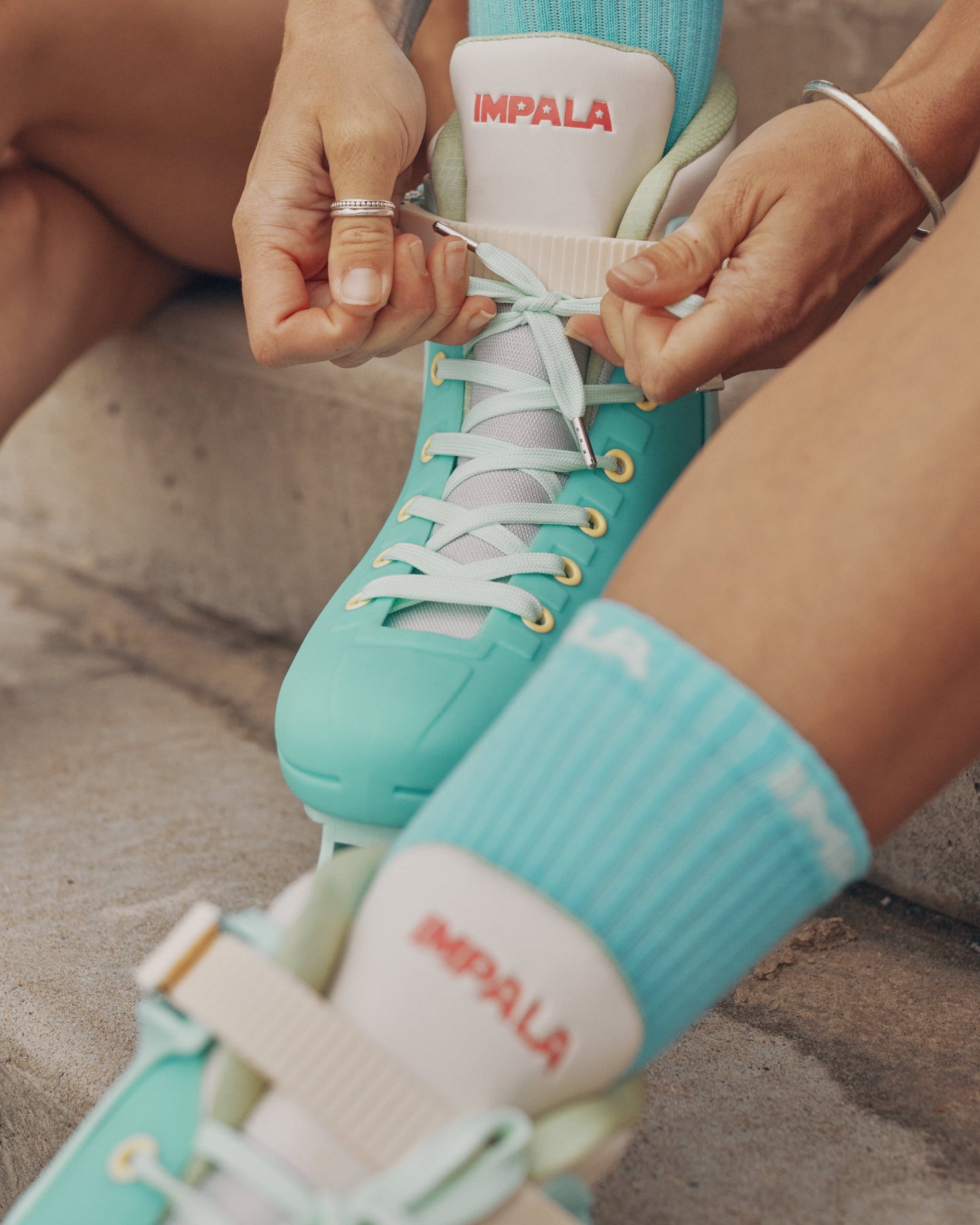 Person tying the laces of teal inline skates with 'Impala' branding.